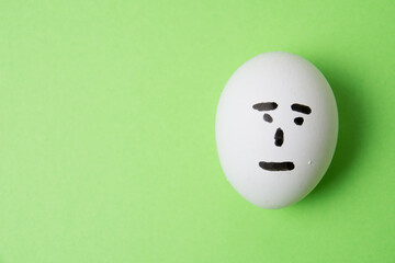 An egg with an indifferent emotion on the face, on a green background copy space.