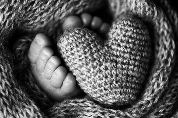 Feet of a newborn with a wooden heart, wrapped in a soft blanket. Black and white studio photography.