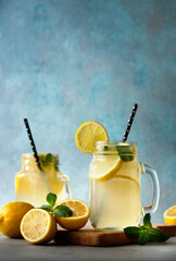 Summer fresh drink with lemons and mint leaves on blue background. Lemonade in jar with straw.
