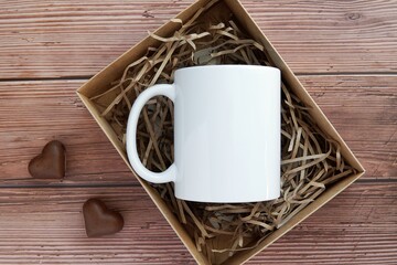 White plain coffee mug mockup in gift box, rustic dark wood background, heart shape chocolate candies, Valentines day gift.