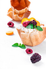 Waffle cup with cottage cheese cream topped with raspberry, blackberry, kumquat and mint on the white table. Homemade dessert