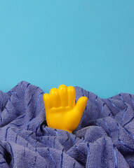 Yellow rubber hand of drowning man on blue towel waves abstract concept photo of turbulent sea or...