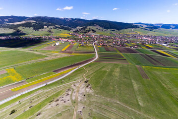 Asphalt road leading through agricultural fields at spring, small hungarian village in the background.