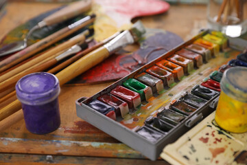 Different paints and brushes on wooden table, closeup