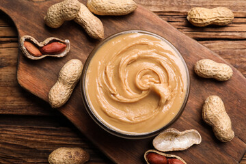 Yummy peanut butter in glass bowl on wooden table, flat lay