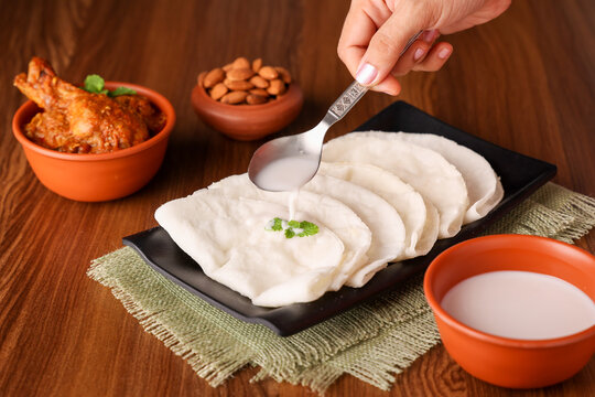 Hand pouring coconut milk on Rice pathiri Pathiri Indian flatbread, chicken curry, Kerala India SriLanka. traditional South Indian breakfast dish Malabar Muslims Ramadan Ramzan, Eid festival Rice roti