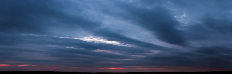 Naklejka na ściany i meble Dark sunset with gloomy clouds and red light on the horizon