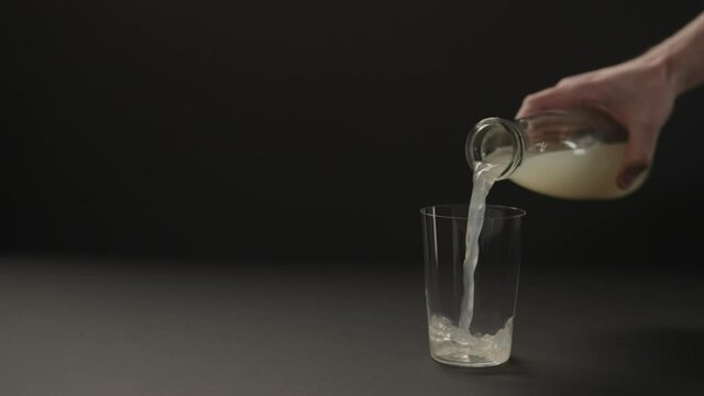Slow motion man hand pour lemon ginger lemonade into tumbler glass on black paper background with copy space