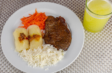 Brazilian food dish with steak and rice and carrot and cassava with eye