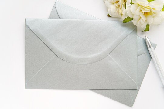 Blank Silver Envelopes For Design, Address Label Or Sticker Presentation, Wedding Envelope Mockup, White Flowers, Pen, Top View.