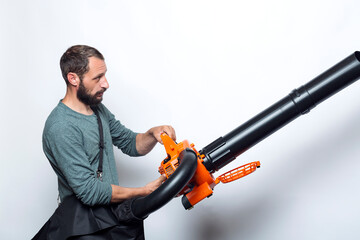 Bearded man holding a Garden blower with a collection bag on white background. Worker with a leaf...