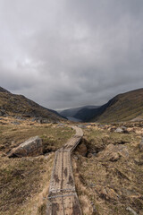 photography of mountainous landscape with wooden path and a lake in the background in Glendalough...