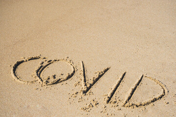 Covid written on the sand of a beach with wave washing the word, erasing or canceling it during Coronavirus summer, Covid free, safe beach, vaccine. Covid-19 immunity passport or pass, bathing season
