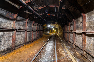 Tunnel of the mining of an underground mine. Lots of pipelines on the ceiling and rail track for...
