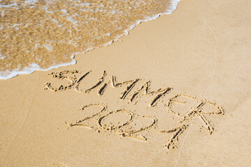 Summer 2021 written on the sand of a beach with wave washing, erasing or canceling it during Coronavirus summer, Covid free, safe beach, vaccine. Covid-19 immunity passport or pass, bathing season
