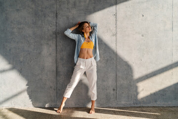 smiling happy beautiful woman posing against concrete wall on sunny day summer fashion style trend