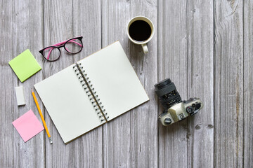Still life, business or traveler memo concept, Top view image of open notebook with vintage camera coffee cup pencil and eyeglasses with blank pages on old brown wooden background, for adding text