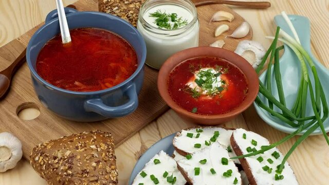 Russian and Ukrainian cuisine. Borscht with sour cream and spices, fresh herbs, garlic and pampushki. Beetroot soup in a blue bowl on a wooden board.