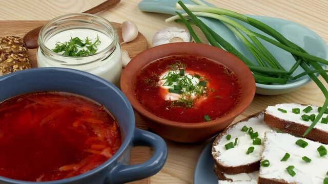 Russian and Ukrainian cuisine. Borscht with sour cream and spices, fresh herbs, garlic and pampushki. Beetroot soup in a blue bowl on a wooden board.