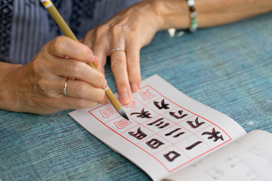 close up hands of senior woman practices eriting calligraphy of traditional chinese characters (focus at tip of brush)