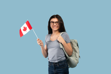 Happy Indian teen exchange student with backpack holding small flag of Canada and smiling at camera...
