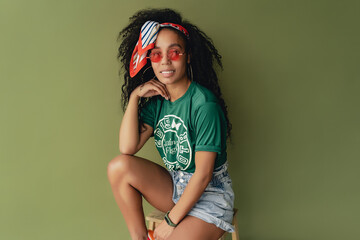 attractive black african american woman posing in stylish hipster outfit on green background