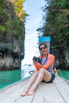 portrait of young asian woman weraing swimsuit holding camera while travel on long tail boat on summer vacation