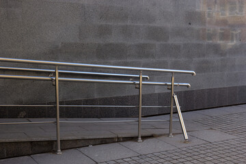 views of the sidewalk, ramp with handrails and a gray wall that reflects the building