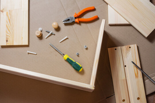Assembly process for wooden furniture. Screws, screwdriver, pliers and wooden parts.