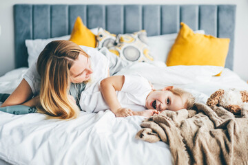 Obraz na płótnie Canvas Happy mother and daughter having fun and playing together on the bed at home.