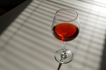 A glass of red wine on a white table with a shade from the blinds