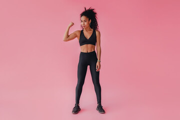 attractive black african american woman in black leggins fitness outfit on pink background