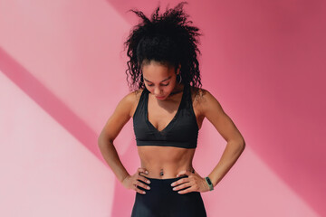 attractive black african american woman in black leggins fitness outfit on pink background