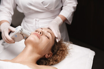 Beauty and body care. Dermatologist hardware cosmetology. Woman client lying at beautician spa salon room and receives SMAS facelift therapy, therapist using ultrasonic device for collagen production