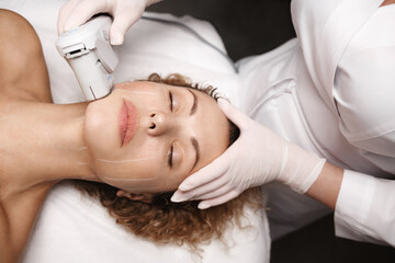 Obraz na płótnie Canvas Spa salon and hardware cosmetology. SMAS non surgical ultrasound facelift procedure carried out by beautician dermatologist in beauty clinic. Ultrasonic device produce collagen on client face skin