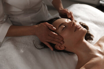 Young woman enjoying massage at spa salon. Beautician rubbing temples of client, smiling girl...