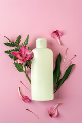Green bottle with moisturizer on pink background with flowers Alstroemeria. Cosmetic container mockup with place for text. Natural skincare beauty product concept.
