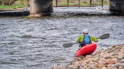 male kayaker wearing drysuit, helmet and life jacket is launching a kayak in the Poudre River Whitewater Park in Fort Collins, Colorado