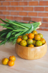 Fresh orange in the wooden bowl put on the wooden table with the pandanus behind. Orange is a healthy fruit and have refreshing sweet taste.