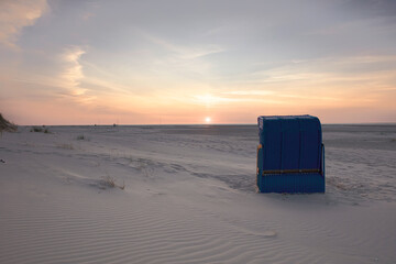 Back view of blue roofed wicker beach chair on empty sand beach at sunset time. Colorful sky.
