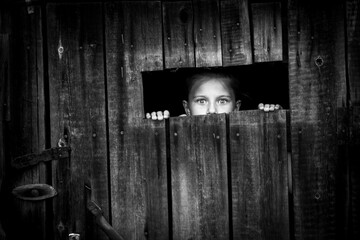 Little girl startled looks out of the shed through a small window.