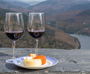 Tasting of Portuguese red dry wine, produced in Douro Valley with goat and sheep cheese and Douro river and terraced vineyards on background in autumn, Portugal