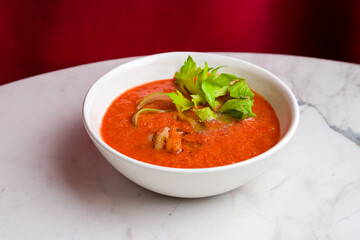 Soup cream of tomato with shrimps and greens on marble table with red curtain back