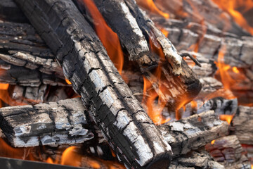 burning firewood stacked in a bonfire with coals in the open air and red flames