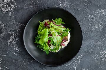 Salad with baked aubergines and feta cheese with greens on black plate top view on dark concrete table