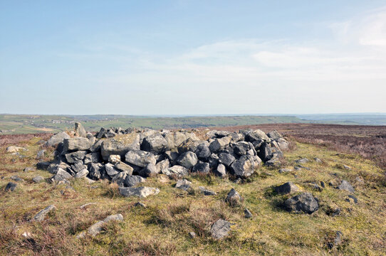the exposed stones at the top of a cairn known as the millers grave on midgley moor in calderdale west yorkshire with the calder valley in the distance