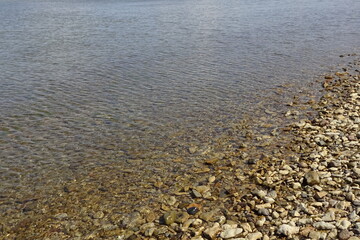 Yellow and brown colors pebble stones' backdrop on the beach in transparent water on a sunny day