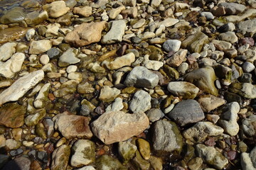The backdrop of gray and brown half wet pebble stones on the beach during a sunny day