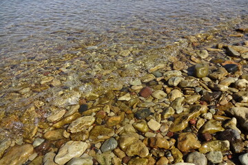 Yellow and brown colors pebble stones' backdrop on the beach in transparent water with a wave coming on a sunny day