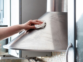 female hand cleans stainless steel kitchen hood